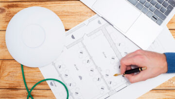 Engineering process. Man developing a network diagram for wifi access in cafe. Access point, floor layout, laptop and man hand on the bright background. Space for your text.