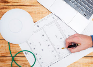 Engineering process. Man developing a network diagram for wifi access in cafe. Access point, floor layout, laptop and man hand on the bright background. Space for your text.
